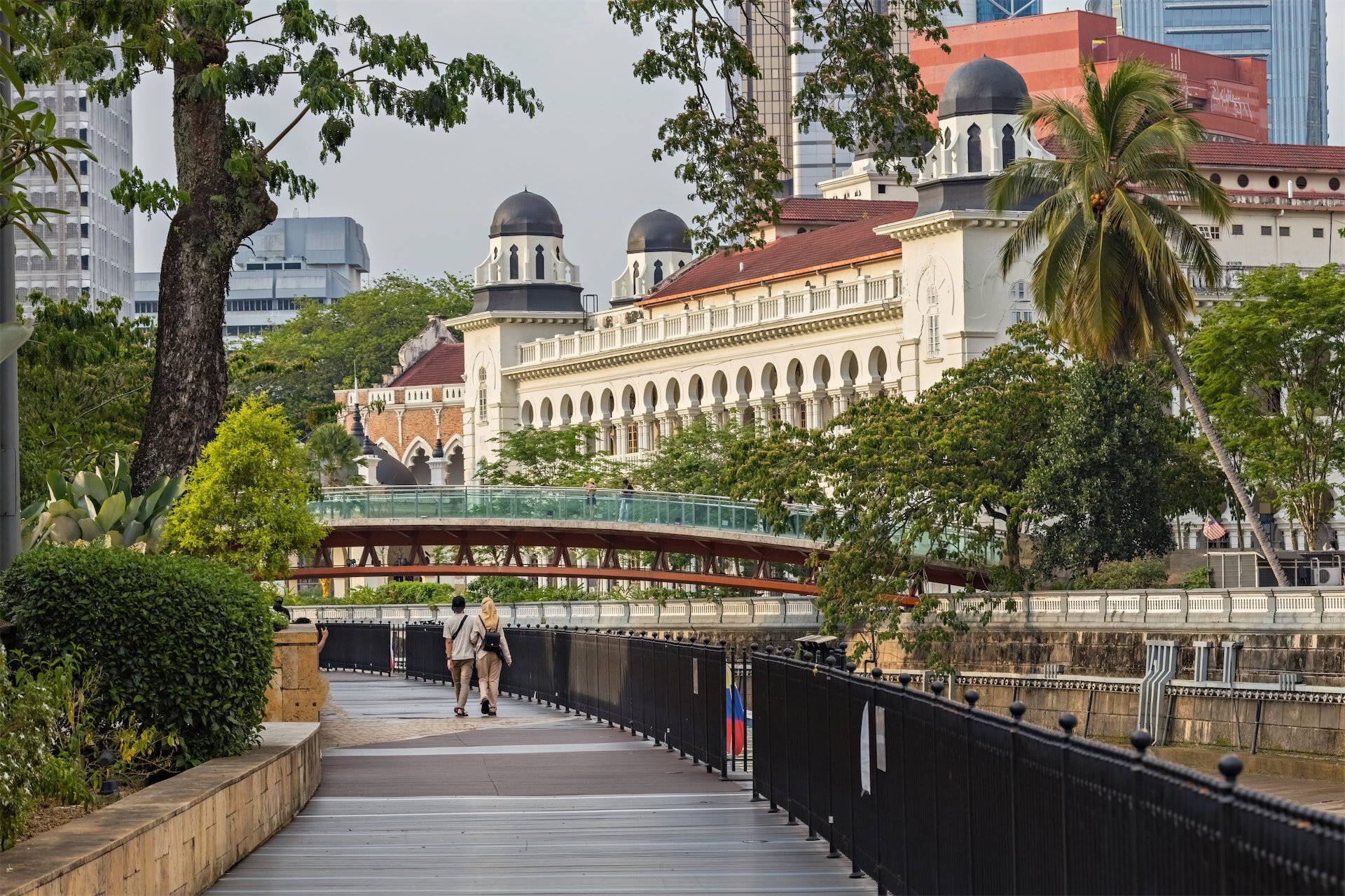 Riverside walk near a curved bridge and heritage domed building, highlighting Kuala Lumpur urban regeneration.