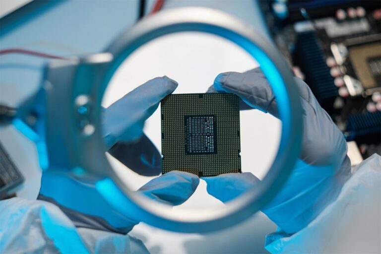 Gloved hands inspect a microchip through a magnifying glass during semiconductor technology R&D.